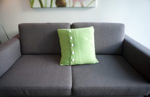 a plain grey sofa with a single green cushion and lots of space for copy
